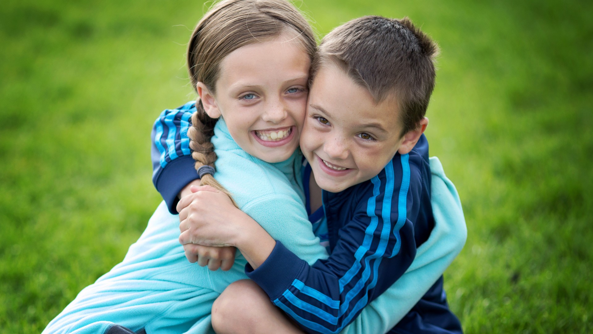 Two smiling Shepherd school-age students hugging outside on the grass